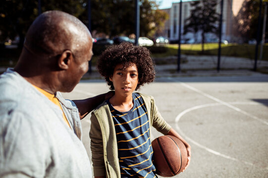 Senior grandfather comforting child grandson on outdoor basketball court