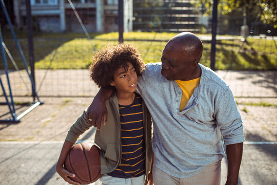 Mature father and teen son sharing supportive moment on basketball court