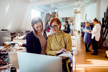 Adult and mature colleagues smiling and focused at computer in fashion studio