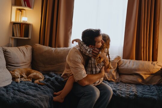 A young father comforts his 4-year-old daughter while reading her a book, sharing a tender moment of paternal love and emotional connection - Powered by Adobe