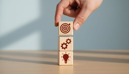 Wooden blocks with target, gears, and lightbulb icons stacked by a hand.