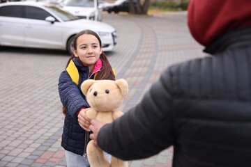 Stranger giving teddy bear to little girl outdoors, closeup. Child in danger