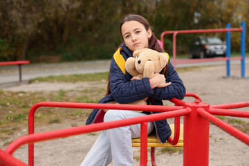 Frustrated girl with teddy bear on merry-go-round at playground