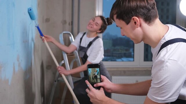 Couple in new home. Man taking photo woman during repair works painting walls. Happy family bloggers painting wall make selfie in social network. Happy family doing home renovation. DIY renew home