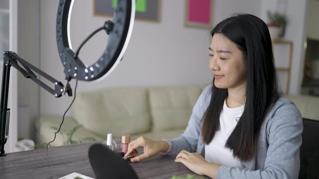 A Thai woman records a makeup vlog at home, speaking confidently to the camera as she demonstrates beauty products and application techniques.