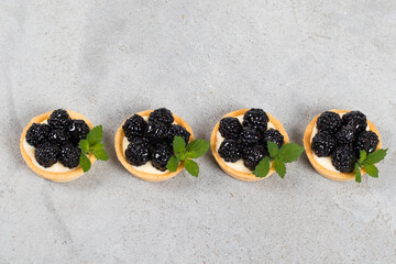 Blackberry round tartlet. Decorated with mint. Light gray background. Top view	
