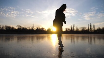 Silhouette of girl shod in figure skates sliding on pond during beautiful sunset. Sportswoman improving skills at lake on freeze day. Shining sun reflecting on surface of ice. Active leisure at winter
