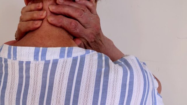 Elderly woman massages her neck and shoulder zone to ease pain and stiffness caused by age and arthritis.