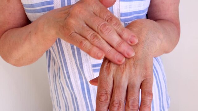 A senior woman gently massages her arthritic hands to ease stiffness, swelling, and age-related discomfort.