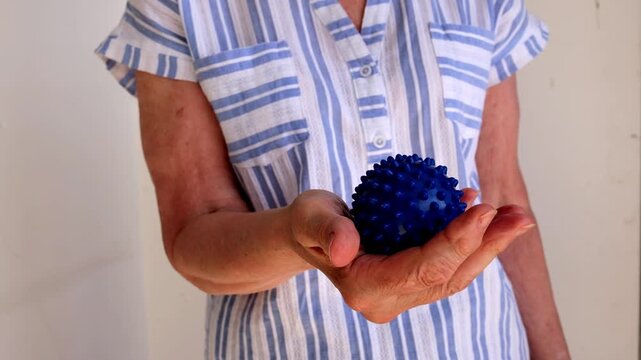 Elderly woman rolls a spiky ball in her hands to ease pain and improve health through gentle self-massage.