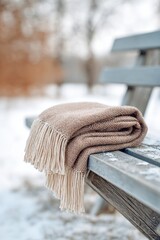 Textured brown blanket draped elegantly over a rustic wooden bench, surrounded by a serene winter landscape, evoking warmth and comfort in a minimalist setting
