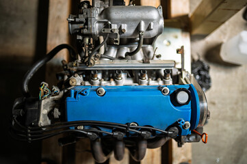 Close-up of a blue-painted Japanese 1.6L SOHC 16-valve internal combustion engine head in a workshop setting. Automotive repair and engineering concept.