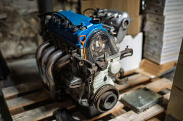Close-up of a blue-painted Japanese 1.6L SOHC 16-valve internal combustion engine head in a workshop setting. Automotive repair and engineering concept.