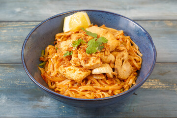 Pad Thaï au poulet dans un bol bleu, cuisine thaïlandaise, fond bleu rustique
