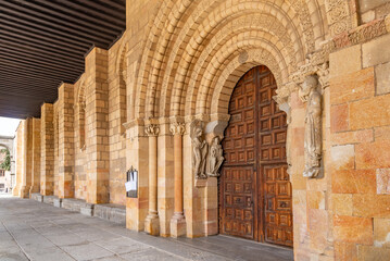 Close-up of Basílica de San Vicente’s Romanesque portal with a large rounded arch, sculpted archivolts on sturdy columns, and massive, richly patterned wooden doors