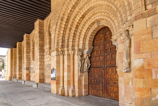 Close-up of Bas&iacute;lica de San Vicente&rsquo;s Romanesque portal with a large rounded arch, sculpted archivolts on sturdy columns, and massive, richly patterned wooden doors