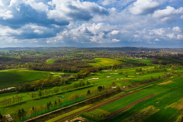 Wide aerial drone panorama of a lush green golf course on a bright, cloudy day. Featuring fairways, sand traps, and luxury resort facilities in the distance.