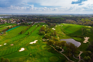 Wide aerial drone panorama of a lush green golf course on a bright, cloudy day. Featuring fairways, sand traps, and luxury resort facilities in the distance.