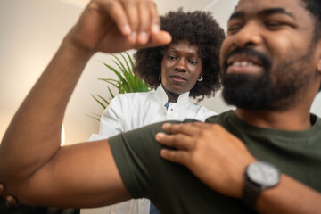 Selective focus of patient sitting on couch and doctor massaging patient shoulder in massage cabinet at clinic