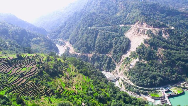 Aerial drone shot panning from step farms on Himalayas to blue waters of Ganga river with a dam blocking the flow to provide hydel power at Chopta Tungnath Uttarakhand India