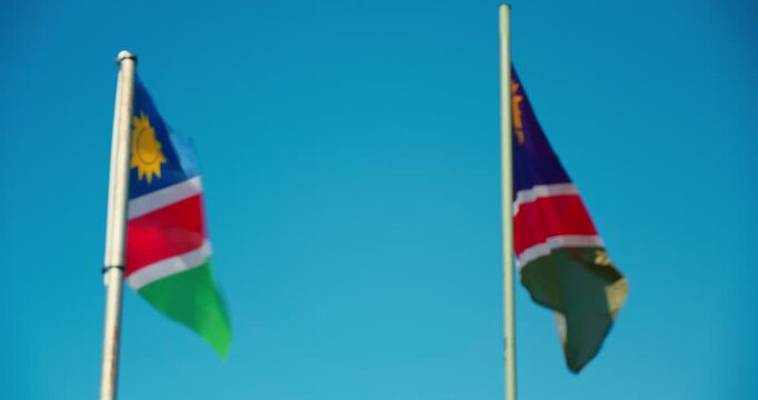 Close-up of two Namibian flags waving in the wind against a clear blue sky, with focus shifting between them, capturing vibrant colors and movement.