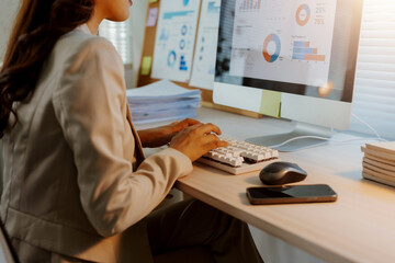 Businesswoman focused on work, typing on a keyboard and analyzing financial charts and data displayed on a computer screen
