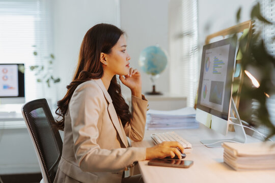 Asian businesswoman working at desk, analyzing charts and graphs on her computer, focused on business data