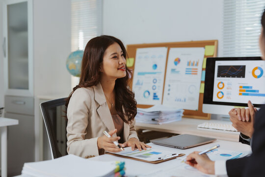 Professional woman holding a pen, discussing financial reports and charts with a colleague during an office business meeting