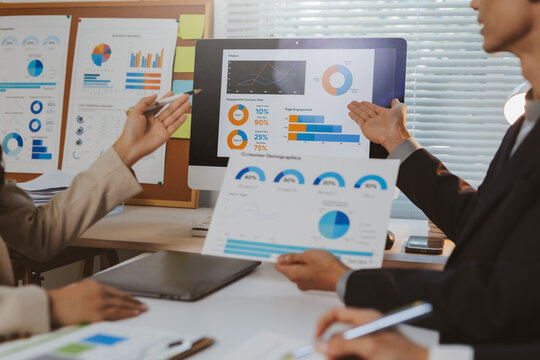 Business colleagues collaborating on a financial report, reviewing data analytics and graphs on a computer screen and paper documents