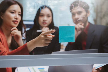 Diverse business team collaborating, brainstorming ideas on a glass board with sticky notes in a modern office meeting