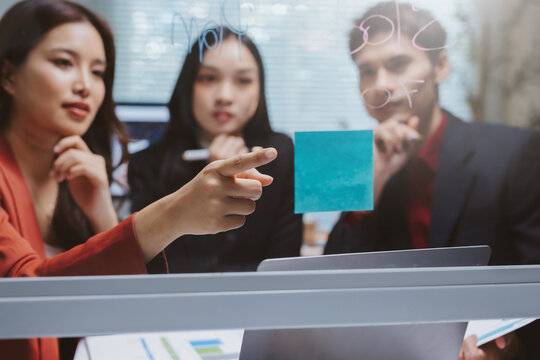 Diverse business team collaborating, brainstorming ideas on a glass board with sticky notes in a modern office meeting