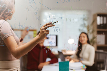 Businesswoman presenting ideas on a glass board during a team meeting, brainstorming strategies and planning projects in a collaborative office