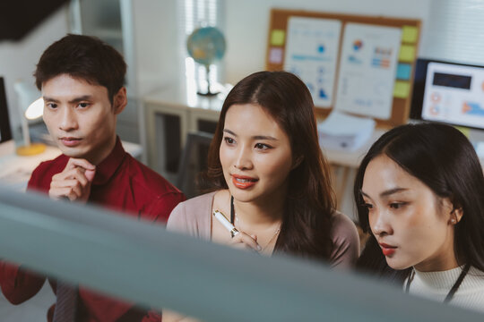 Young Asian business professionals collaborating in a modern office, analyzing data and discussing strategy on a computer screen