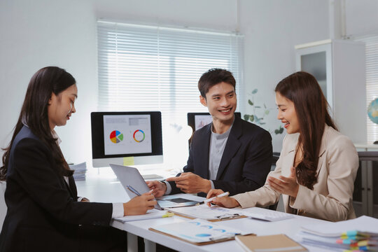 Asian business professionals discussing financial reports and charts, collaborating on a project in a modern office environment