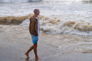 young Man stands in foamy ocean waves, male finds peace standing in surf, letting rhythm waves wash away worries, wearing shorts and jacket, embodying serenity, connection to nature, coastal escape