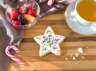 Sweet Indulgence: A delightful star-shaped cookie, adorned with colorful sprinkles, sits alongside a vibrant fruit bowl, a warm cup of tea, and a festive candy cane.