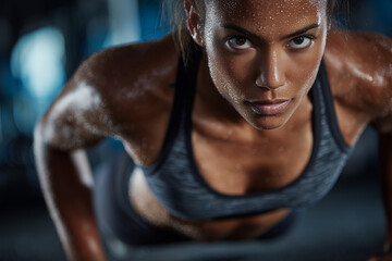 Sweaty athletic woman holding a plank position in a gym, looking focused and determined, illustrating core strength, endurance, and dedication to fitness.