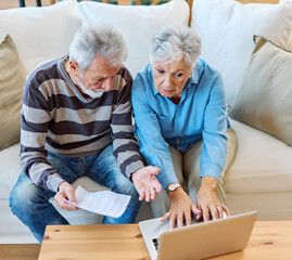 Senior couple checking bills and calculating expenses using a laptop at home, debt taxes concept, worried married elderly couple