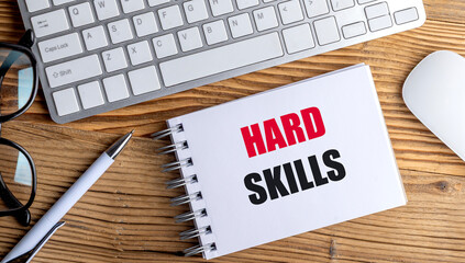Hard skills phrase written on notebook with pen, keyboard, glasses and mouse on wooden desktop