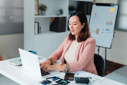 Asian businesswoman typing on laptop and looking at data analysis charts, focusing on business information and digital work in office