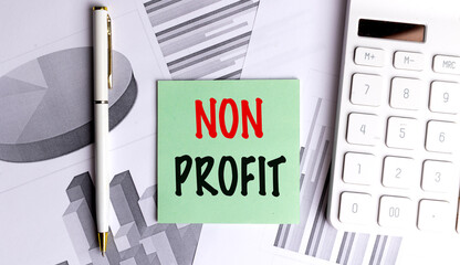 Non profit message on green note with charts, pen and calculator on office desk background