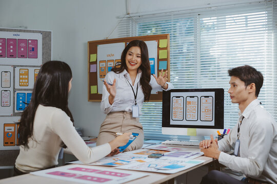 Team of UIUX designers collaborating on mobile app wireframes and user interface designs, discussing project strategy in an office