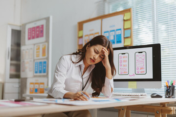 Professional woman suffering a headache and feeling overwhelmed by work designing user experience and wireframes in an office