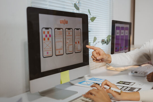 UXUI designers working together, pointing at computer screen displaying responsive mobile application wireframes and mockups for new project
