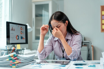 Young businesswoman feeling overwhelmed and stressed from work, suffering from headache and eye strain at her desk