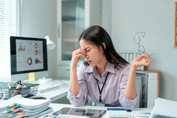 Asian businesswoman feeling tired and stressed, having a headache while working at office desk. Experiencing burnout from overwork and computer