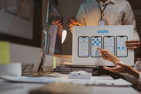 Professional team collaborating on mobile user experience and user interface development, analyzing wireframes and design mockups - Powered by Adobe