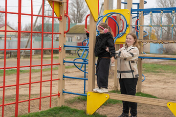 Mother supporting daughter balancing on playground climbing frame, joyful family moment
