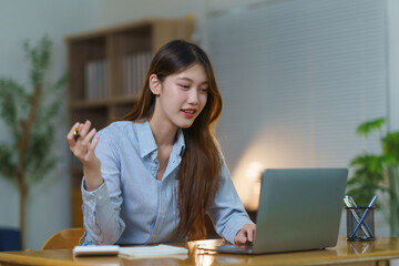 Asian woman using laptop for online video call meeting, working from home or studying remotely at her desk