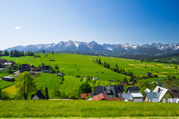 Panoramic view of the snow-capped Tatra Mountains from Rzepiska village in Podhale, Poland. Scenic June landscape with vivid green fields and rural settlement.